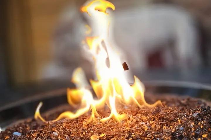 Close-up of gas flames rising over amber fire glass in a fire pit