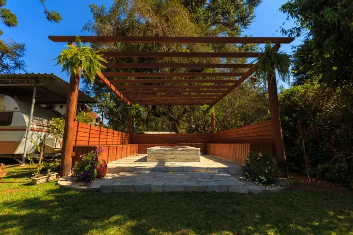 A timber pergola over a natural stone patio with a stacked-stone fire feature