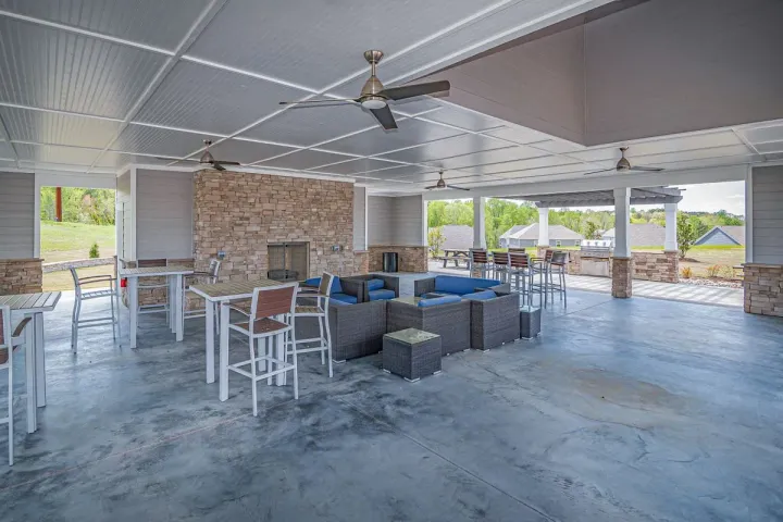 A large roofed pavilion outdoor room with a stone fireplace, ceiling fans, and lounge seating